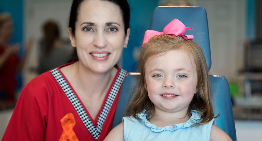 A child and a dental hygienist smiling during a pediatric dentistry appointment.